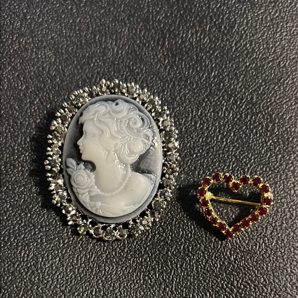 One blueish Cameo Brooch and a Tiny red heart pin.  Both in new condition.